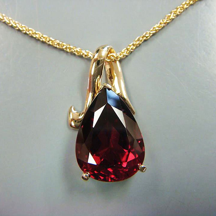 Handmade pendant with a deep red pear-shaped gemstone and a sculpted yellow gold bail, by Arendsen Jewelers