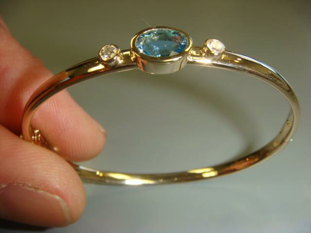 Two-tone gold bangle with a bezel-set light blue gemstone