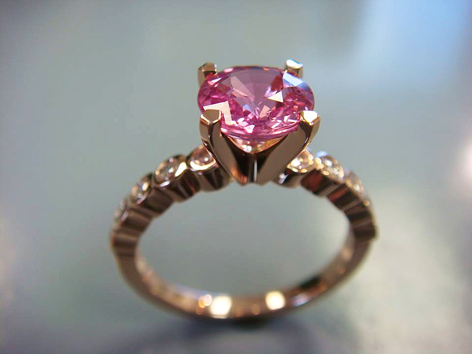 Gold engagement ring with a round pink gemstone and a diamond-set band