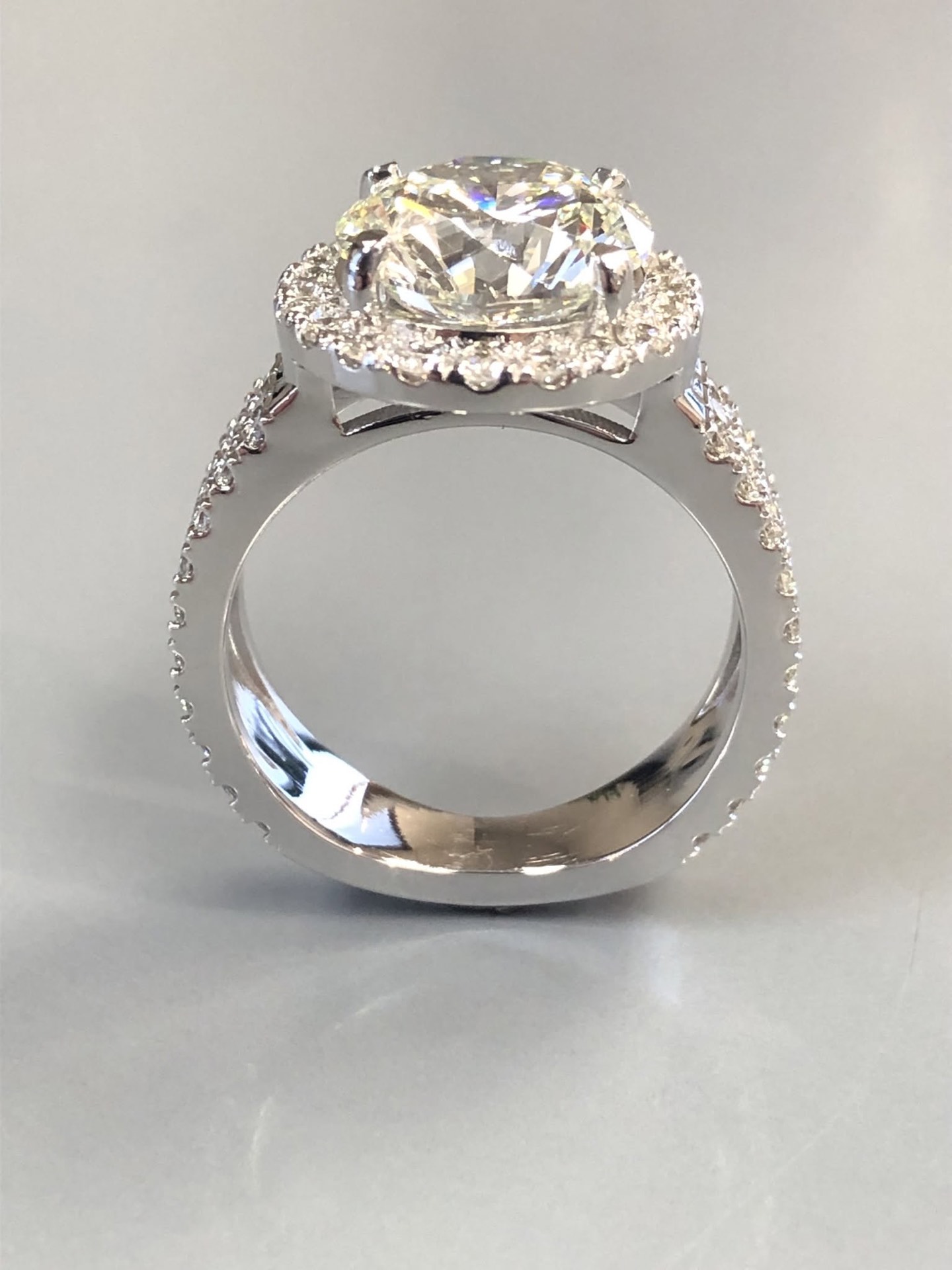 White gold halo engagement ring with a round diamond and a pavé band