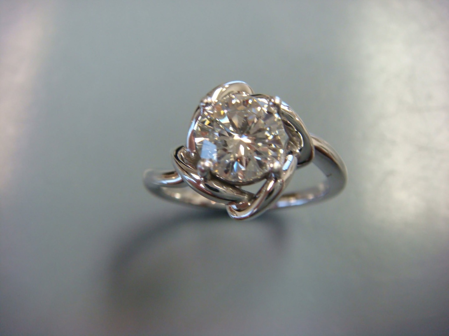 White gold engagement ring with a round diamond cradled in swirling bands
