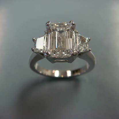 White gold three-stone ring with an emerald-cut diamond and trapezoid sides