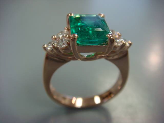 Emerald-cut green gemstone with diamond side stones on a gold band