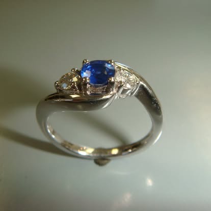 White gold bypass ring with an oval blue sapphire and a diamond
