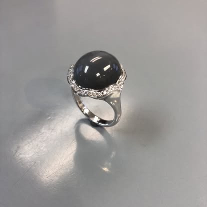 White gold ring with a dark round cabochon and diamond accents