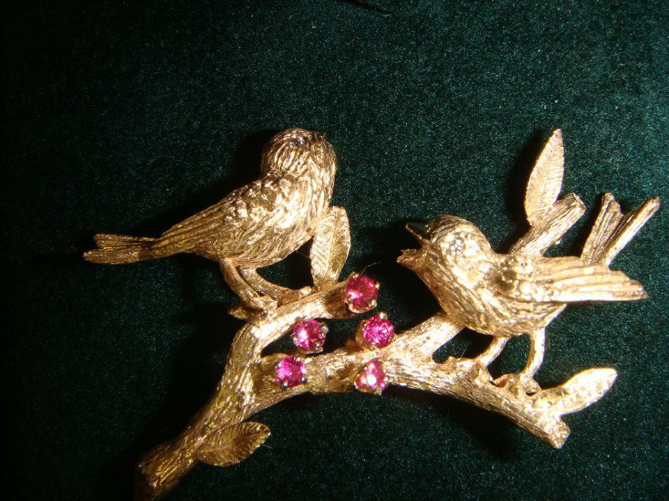 Hand-carved gold brooch of two birds on a branch with pink gemstone berries