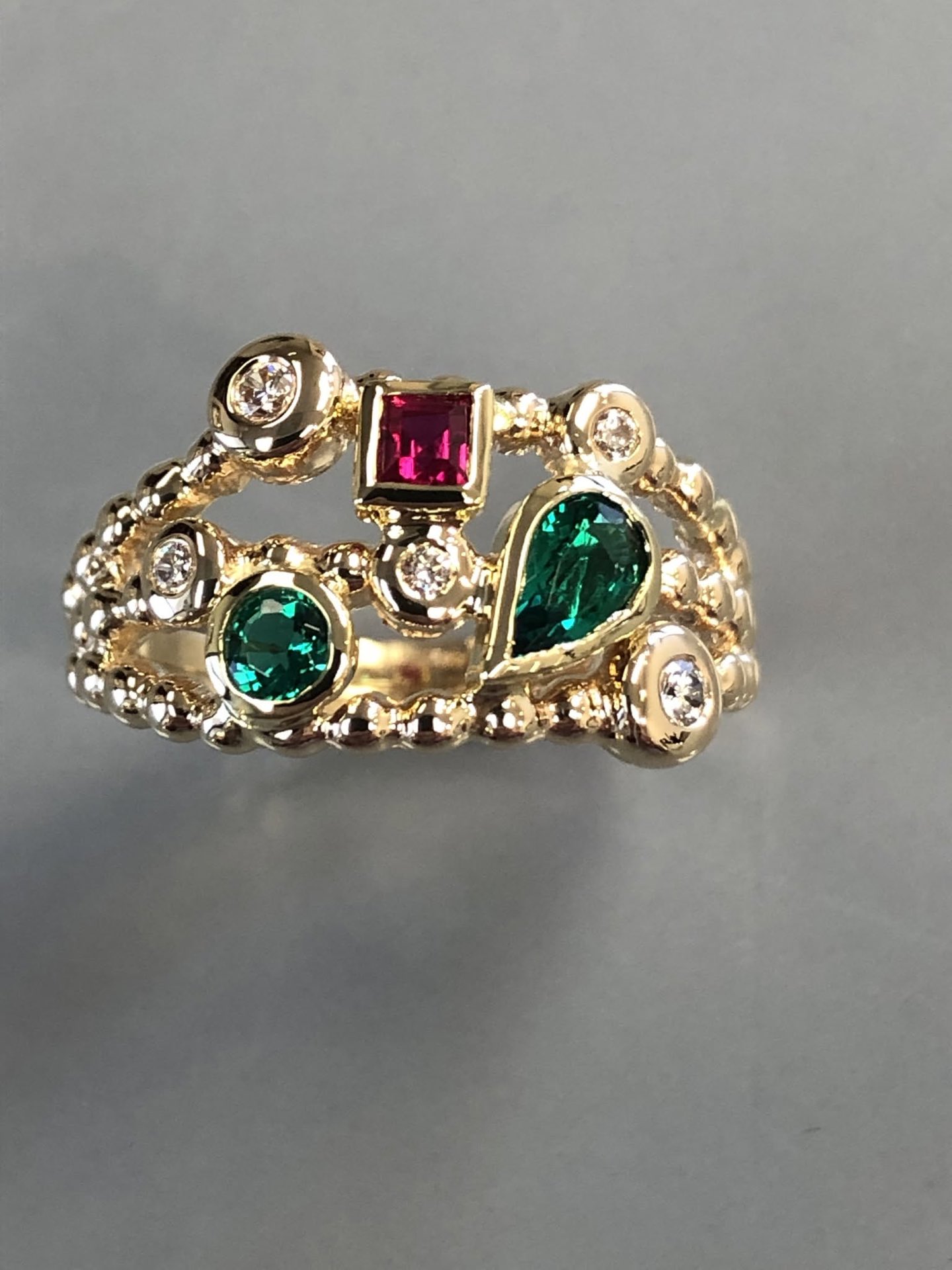 Handmade gold ring set with emeralds, a ruby and bezel-set diamonds