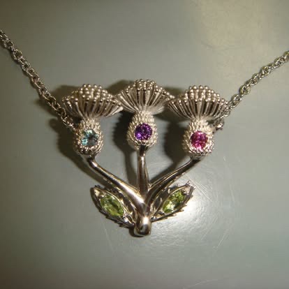 Handmade thistle brooch in gold with purple and pink gemstones