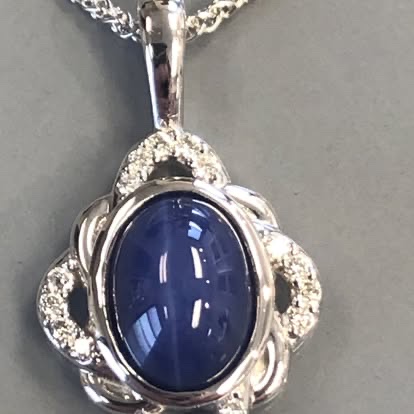 Blue star sapphire cabochon pendant in a white gold scroll frame