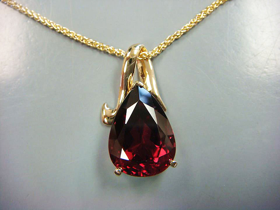 Pear-shaped red gemstone pendant with a sculpted yellow gold bail
