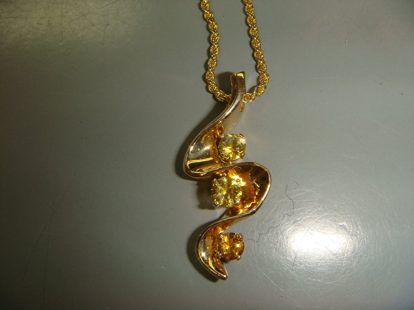Sculptural gold pendant with three yellow gemstones on a gold rope chain