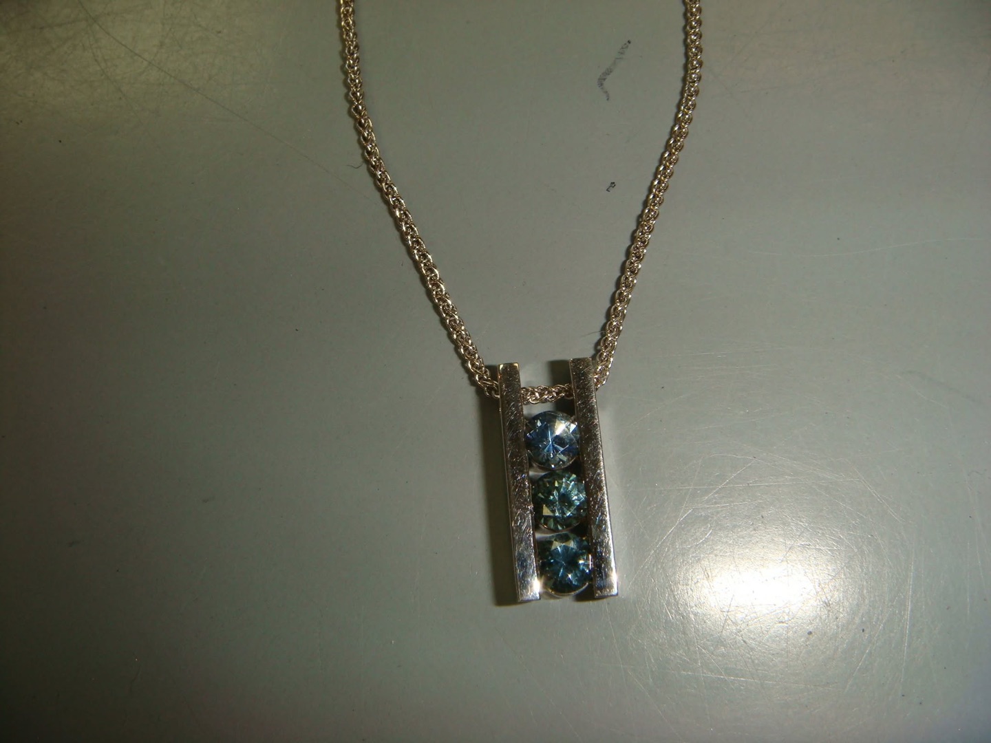 White gold bar pendant with three channel-set blue gemstones